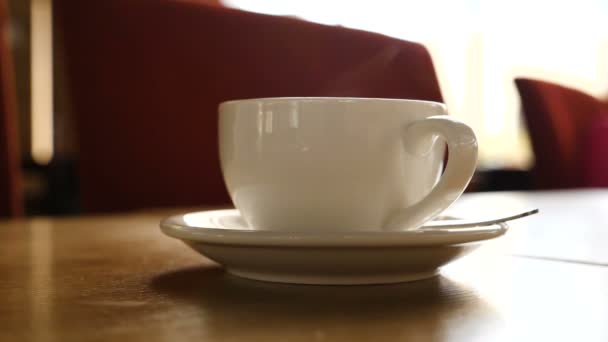 Een hete dampende mok koffie met wazig mensen bewegen op de achtergrond. — Stockvideo