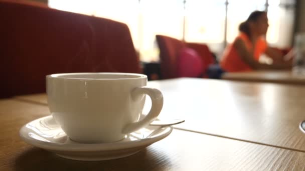 Uma caneca quente fumegante de café com pessoas desfocadas se movendo no fundo . — Vídeo de Stock