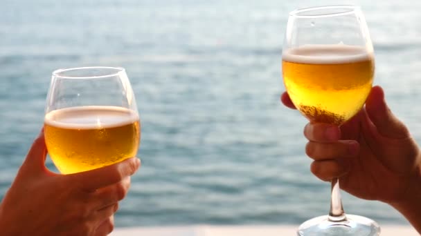 Два человека звонят в стаканы с алкоголем на фоне моря. Крупный план, замедленная съемка — стоковое видео
