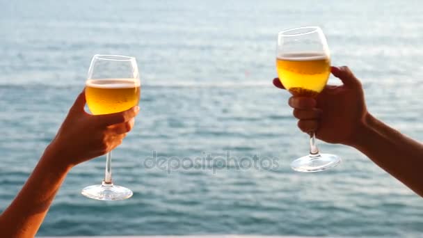 Два человека звонят в стаканы с алкоголем на фоне моря. Крупный план, замедленная съемка — стоковое видео