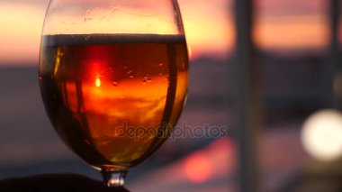 Bir adam bir bardak alkol karşı günbatımı deniz tutuyor. yakın çekim. Ağır çekim