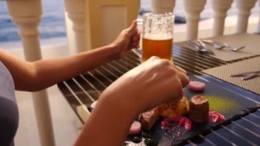 Sahil Restoran. Bir kadın et yiyor ve bir restoranda bira içiyor. Ağır çekim. yakın çekim