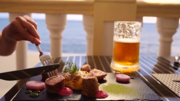 Ristorante sul mare. Una donna mangia carne e beve birra in un ristorante. Al rallentatore. primo piano — Video Stock