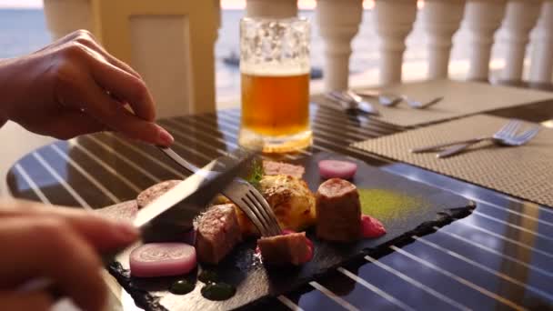 Ristorante sul mare. Una donna mangia carne e beve birra in un ristorante. Al rallentatore. primo piano — Video Stock