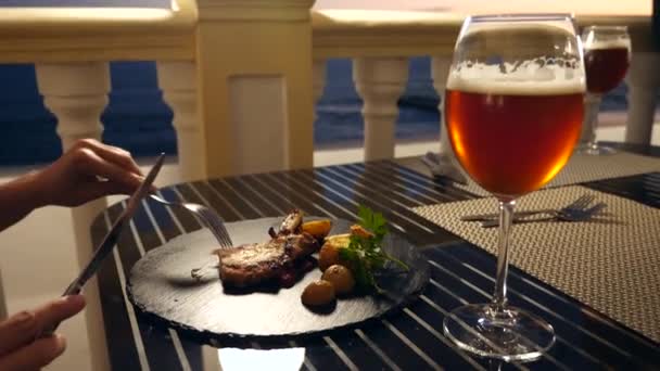 Ristorante sul mare. Una donna mangia carne e beve birra in un ristorante. Al rallentatore. primo piano — Video Stock