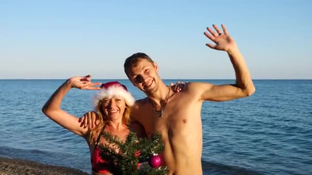 Coppia ragazzo e ragazza in cappello di Babbo Natale salutato il nuovo anno e Natale sulla spiaggia. Decorare un albero di Natale su una spiaggia tropicale. Rallentatore — Video Stock