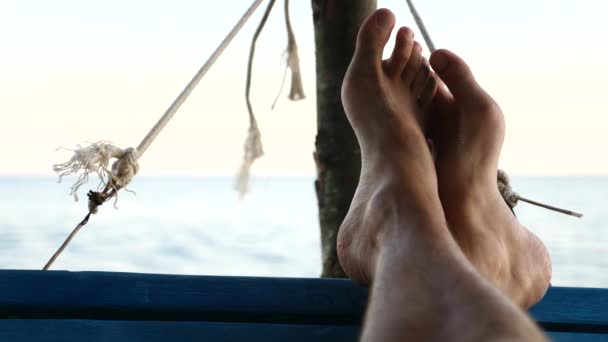 Pies balanceándose en una hamaca, Relajándose en la playa al atardecer. cámara lenta — Vídeo de stock