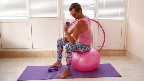 Um cara bonito brincalhão em uma camiseta rosa e leggings azuis está envolvido na aptidão retratando uma menina. Movimento lento — Vídeo de Stock