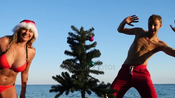 Pareja chico y chica en sombrero de santa saludó el año nuevo y la Navidad en la playa. Para decorar un árbol de Navidad en una playa tropical. Movimiento lento — Vídeos de Stock