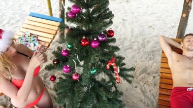 İki adam ve Noel Baba şapkalı kız Noel ve yeni yıl sahilde karşıladı. Tropikal bir plajda bir Noel ağacı süslemek için. Ağır çekim