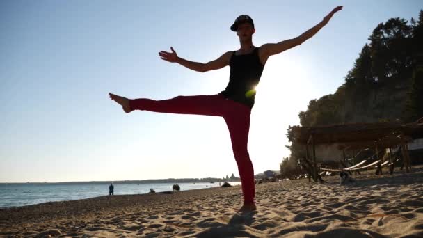 Молодой счастливый парень танцует современный балет и дрочит на песчаном пляже на фоне моря. Slow-mo — стоковое видео