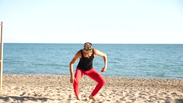 Un giovane ragazzo felice che balla balletto moderno e si masturba su una spiaggia di sabbia sullo sfondo del mare. Lentamente. — Video Stock