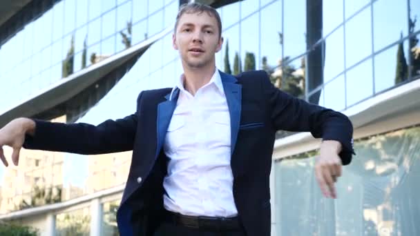 Ein junger, glücklicher Geschäftsmann in einem Business-Anzug, der vor der Kulisse eines Business-Centers modernes Ballett tanzt. Zeitlupe — Stockvideo
