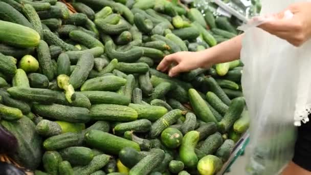 Een vrouw in een supermarkt op een plantaardige plank, koopt groenten en fruit. Man kiest komkommer. Slow motion — Stockvideo