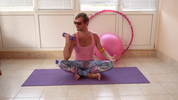 Un bel ragazzo giocherellone con una t-shirt rosa e leggings blu è impegnato in fitness raffigurante una ragazza. Rallentatore — Video Stock