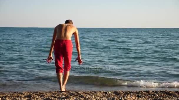 Ein junger glücklicher Kerl, der modernes Ballett tanzt und an einem Sandstrand vor dem Hintergrund des Meeres schläft. Zeitlupe — Stockvideo