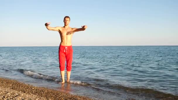 A young happy guy dancing modern ballet and wacking on a sandy beach on the background of the sea. Slow-mo