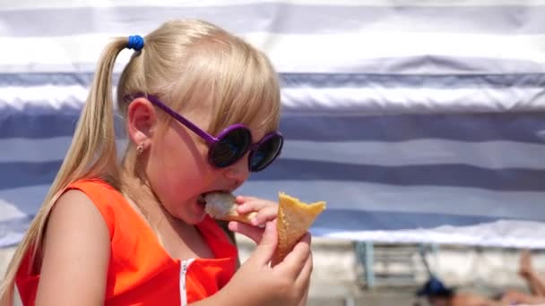 Blonďatá holčička jíst ovoce zmrzlina na pláži v za jasného slunečného dne. 4 k. Zpomalený pohyb. — Stock video
