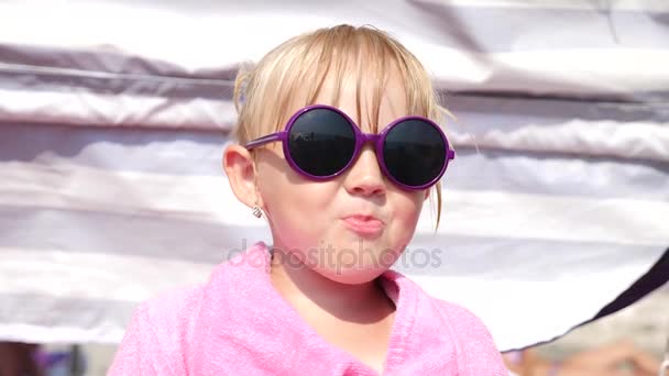 Blonďatá holčička v sluneční brýle jíst ovoce na pláži. 4 k. Zpomalený pohyb. — Stock video