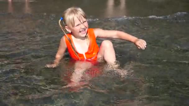 Niña rubia de 3 años sentada en la playa y disfrutando de la ola. En cámara lenta. 4K — Vídeos de Stock