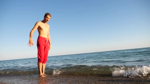 A young happy guy dancing modern ballet and wacking on a sandy beach on the background of the sea. Slow-mo — Stock Video