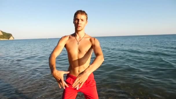 一个年轻的快乐的人在沙滩上的大海背景上跳舞现代芭蕾舞剧和 wacking。慢动作 — 图库视频影像