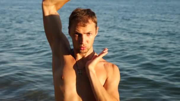 Um jovem feliz dançando balé moderno e wacking em uma praia de areia no fundo do mar. Devagar. — Vídeo de Stock