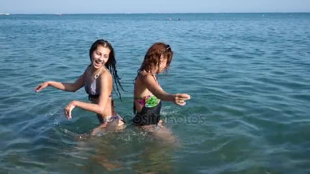 Due ragazze sexy, bruna e dai capelli rossi si stanno divertendo nel mare. Cospargetevi d'acqua e divertitevi. Al rallentatore. 4K . — Video Stock