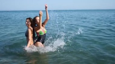 İki seksi kız arkadaşım, esmer ve Kızıl saçlı kendilerini denizin tadını çıkarıyor. Birbirlerine su ile serpin ve eğlenin. Ağır çekim. 4k.