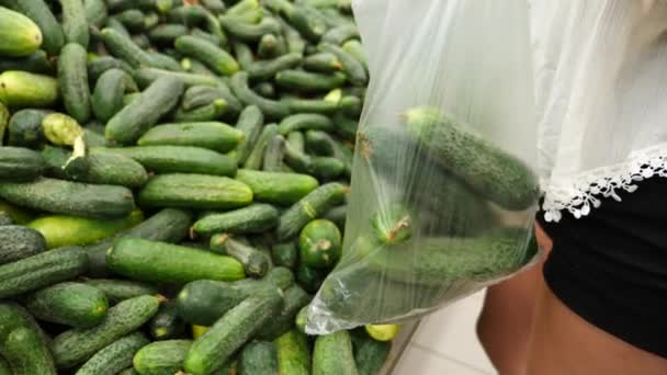 Een vrouw in een supermarkt op een plantaardige plank, koopt groenten en fruit. Man kiest komkommer. Slow motion — Stockvideo