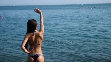 Bikinili seksi kız denizde kameraya onu geri ile ayakta su sıçramalarına, onun ince rakam ve elastik kalça görülebilir. Ağır çekim, 4k.
