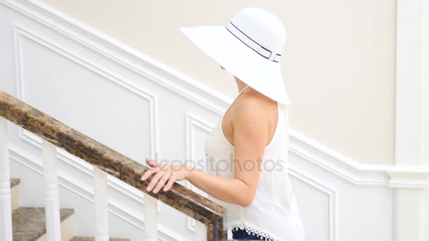 En kvinna i en stor vit hatt går ner en stor vit trappa. 4 k. slowmotion — Stockvideo