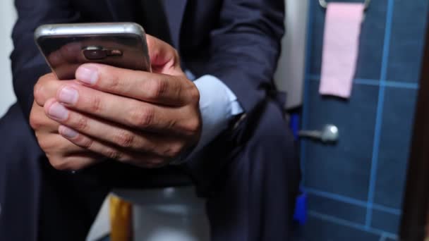 Männliche Geschäftsmann sieht die Nachrichten am Telefon auf der Toilette sitzend. 4k — Stockvideo