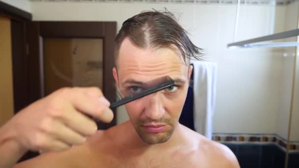 Молодой привлекательный мужчина осматривает отступающую линию волос в ванной. Лысина. 4k, slow motion — стоковое видео