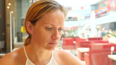 Sarışın bir kadın bir sıcak yaz gününde bir kafede oturan ve üzerinde telefon gülümseyen bir iletide metin yazarak. 4 k. Slow-motion