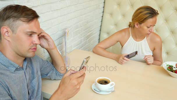 Um casal no café. Homem e mulher bonita num encontro. Estão todos a olhar para o telemóvel dele. 4K. Movimento lento — Vídeo de Stock