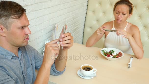 Couple dans un café. Homme et belle femme à un rendez-vous. Tout le monde regarde son portable. 4k. Mouvement lent — Video