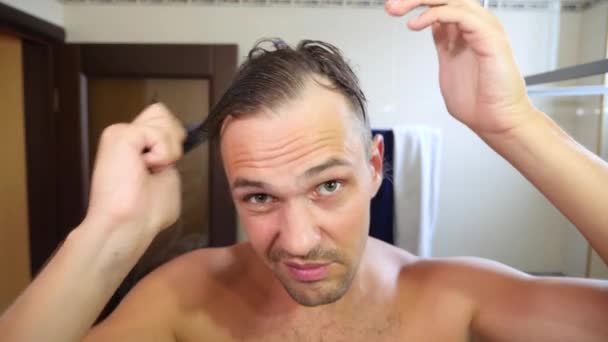 Homem atraente jovem inspeciona uma linha de cabelo recuando no banheiro. Calvície. 4k, câmera lenta — Vídeo de Stock