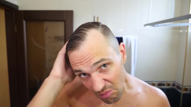 Mladý atraktivní muž kontroluje ustupující vlasovou linkou, v koupelně. Plešatost. 4k, pomalý pohyb — Stock video