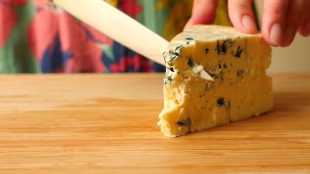 Les mains féminines avec un couteau découpent le fromage avec un moule bleu sur une planche en bois. 4k. Mouvement lent — Video