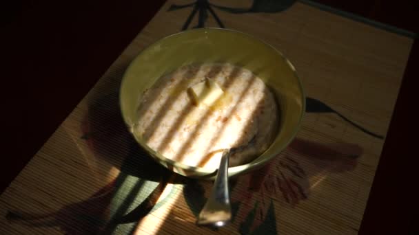 Тарелка с овсянкой и плавильным маслом. На фоне тени от жалюзи. Завтрак дома. 4k. Съемка замедленного действия — стоковое видео