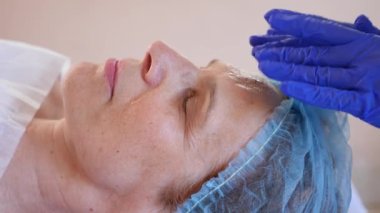 Yaşlı kadın yüz maskesi alma için Spa terapi. 4 k. ağır çekim. Bir güzellik uzmanı alımı