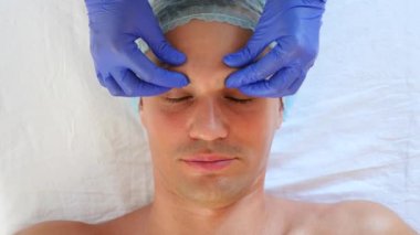 Yakışıklı erkekler yüz maskesi alma için spa terapisi. 4 k. ağır çekim. Bir güzellik uzmanı alımı