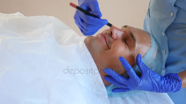El esteticista hace marcas en la cara de un hombre con un lápiz. Cirugía plástica. Cara de contorno de plástico para hombres. 4k. Disparo lento . — Vídeos de Stock