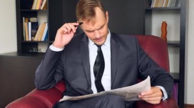 İşadamı bir sandalyede oturuyor ve bir gazete okuyor. O mutsuz ve etkileyici. 4. Ağır çekim.