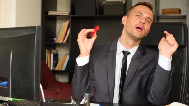 Roter Handspinner oder zappelnder Spinner, der sich auf seiner Hand dreht. Mann im Anzug, der in seinem Büro an seinem Schreibtisch einen Fidget Spinner dreht. Verdrehungen auf der Nase. 4k. Zeitlupe — Stockvideo