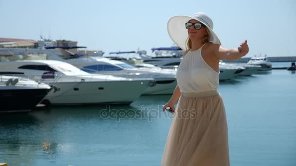 Mujer en sombrero y gafas de sol en el fondo hace bahía selfie con yates. La muchacha en la falda-el sol está girando y regocijándose. 4k cámara lenta . — Vídeos de Stock