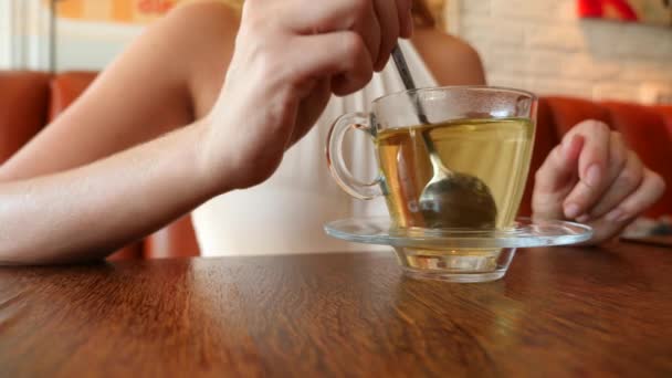 Het meisje roert suiker in een transparante mok met groene thee. 4k, slow-motion. — Stockvideo