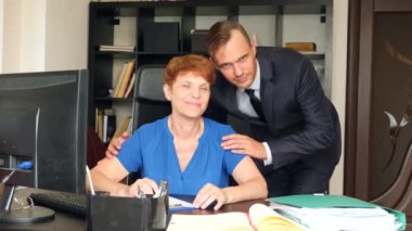 Yaşlı Anne ofiste masasında oturuyor. Onun oğlu bir işadamı onu arkadan sarılarak ve gülümsüyor. Aile şirketi. 4 k. ağır çekim.