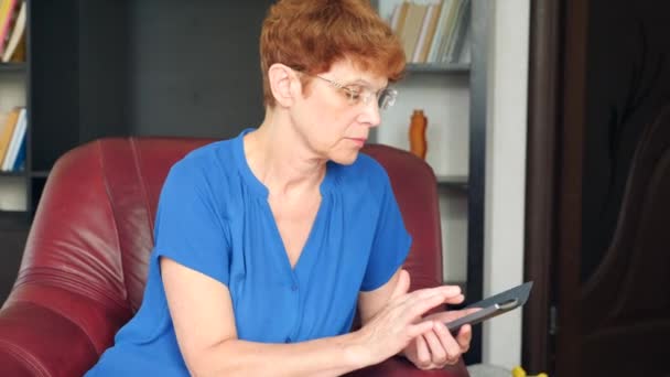 La anciana sentada en una silla de cuero marca un mensaje en su teléfono inteligente. 4k, cámara lenta — Vídeos de Stock
